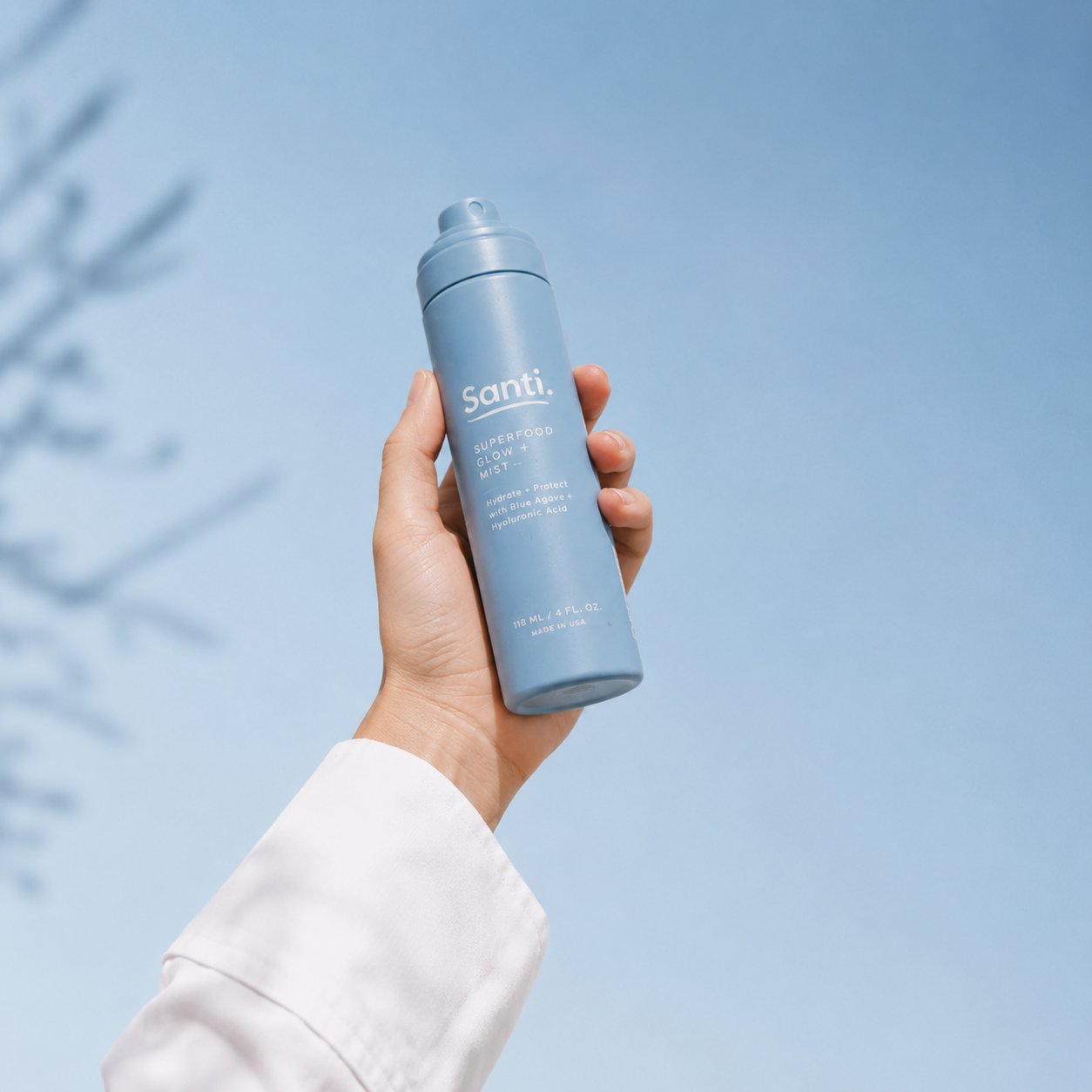 Santi mist bottle held up against the sky with soft leaf shadows
